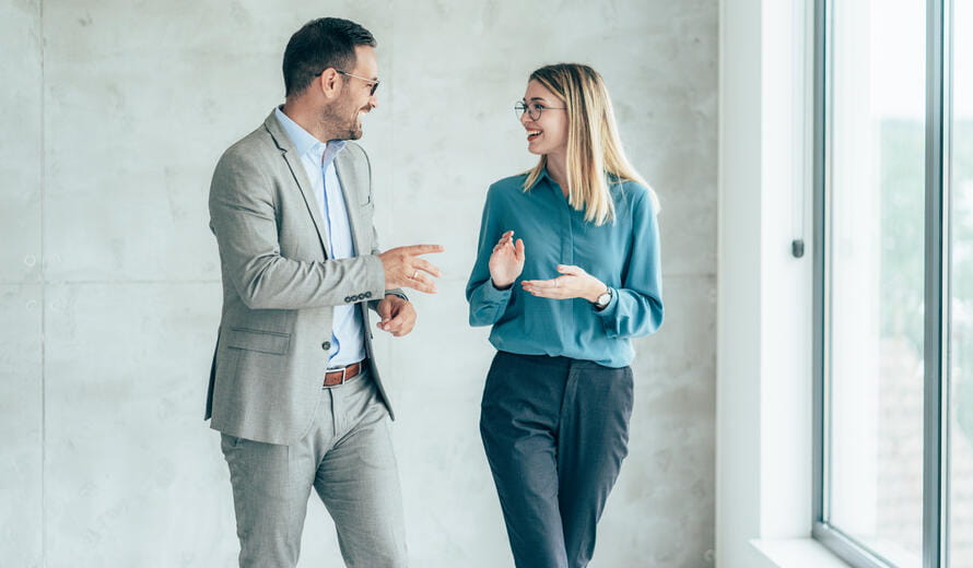 Two smiling business people walking through office hall and talking