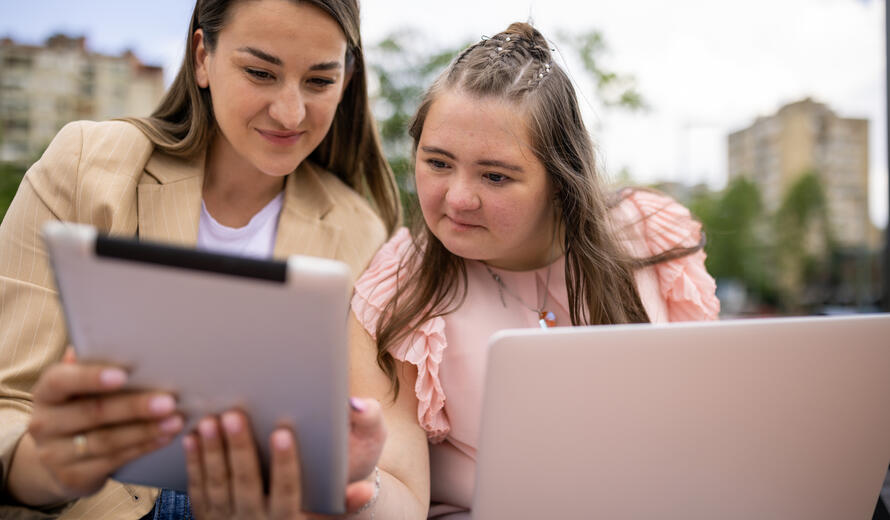 Two women, one with down syndrome using digital devices in a public park together