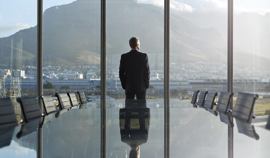  Portrait of male CEO in big corner office, looking out of window, at sunset