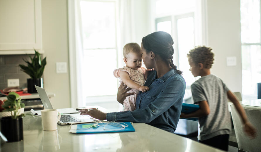 Mother holding baby while using laptop/working from home